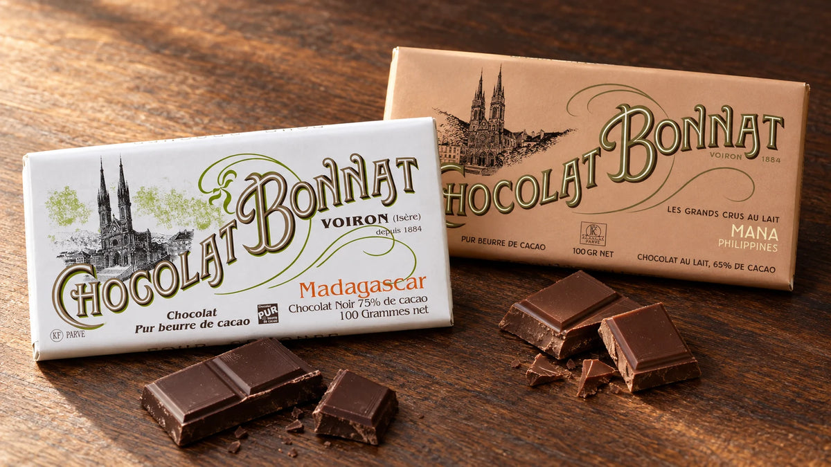 Tablettes Bonnat Madagascar et Mana mises en scène avec des morceaux de chocolat sur une table en bois.